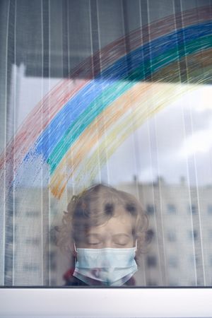 Boy in medical mask standing near window