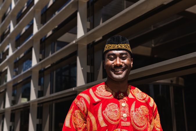 Smiling Black man in traditional clothes and headdress near building