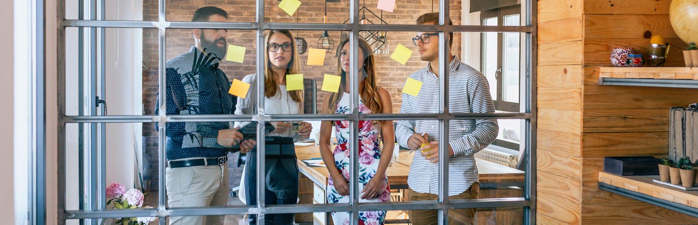 Business people in a work meeting placing sticky notes on the wa