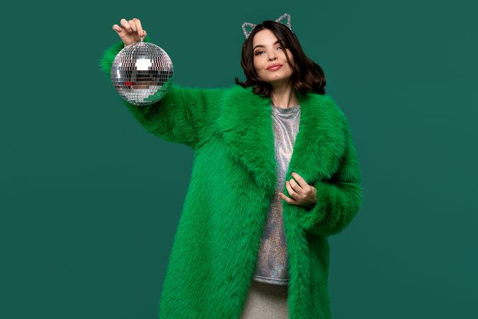 Fashionable woman in green fur coat posing with disco ball.