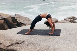 Female stretching her back in bridge pose while next to the ocean