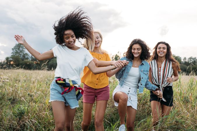 Four happy women hold hands and running on a field