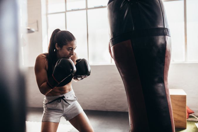 Athletic female boxer using a punching bag with gloves inside a boxing ring