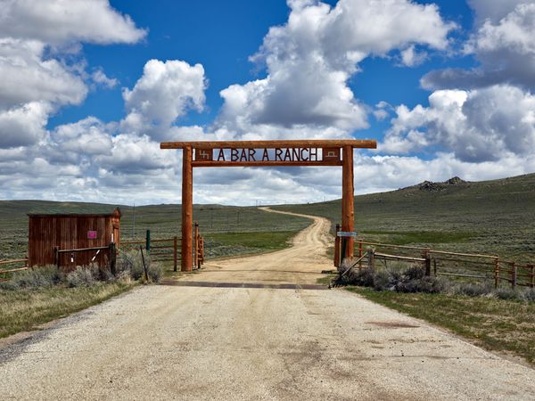 Ranch gate stop a rural road against blue cloudy sky outside Riverside, Wyoming