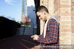 Young bearded male leaning on a brick wall while using a smartphone bDjZmp