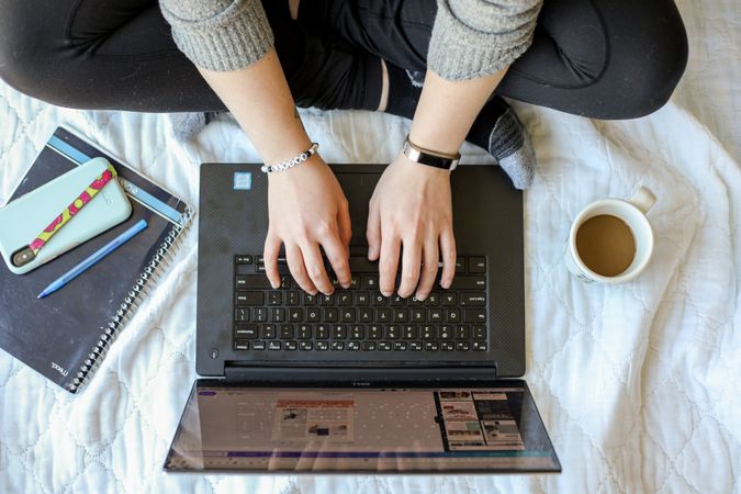 Woman working on laptop in bed beside cup of coffee