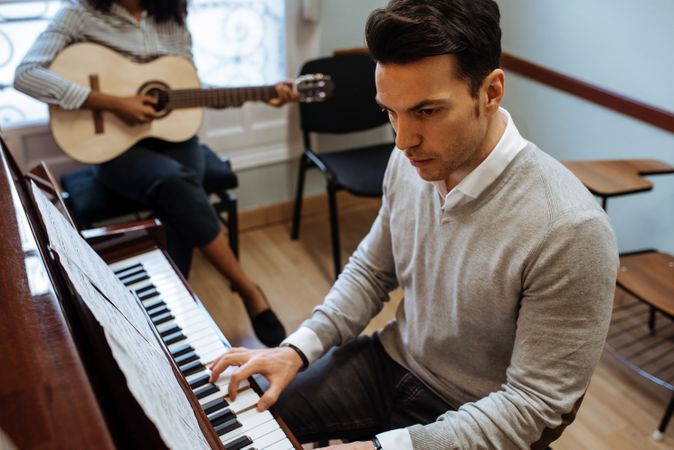 Man playing piano near woman playing guitar in studio