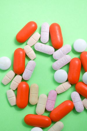 Prescription pills and vitamins scattered on green background with copy space and vertical composition