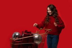 Smiling girl in red sweater pushes shopping cart with gifts