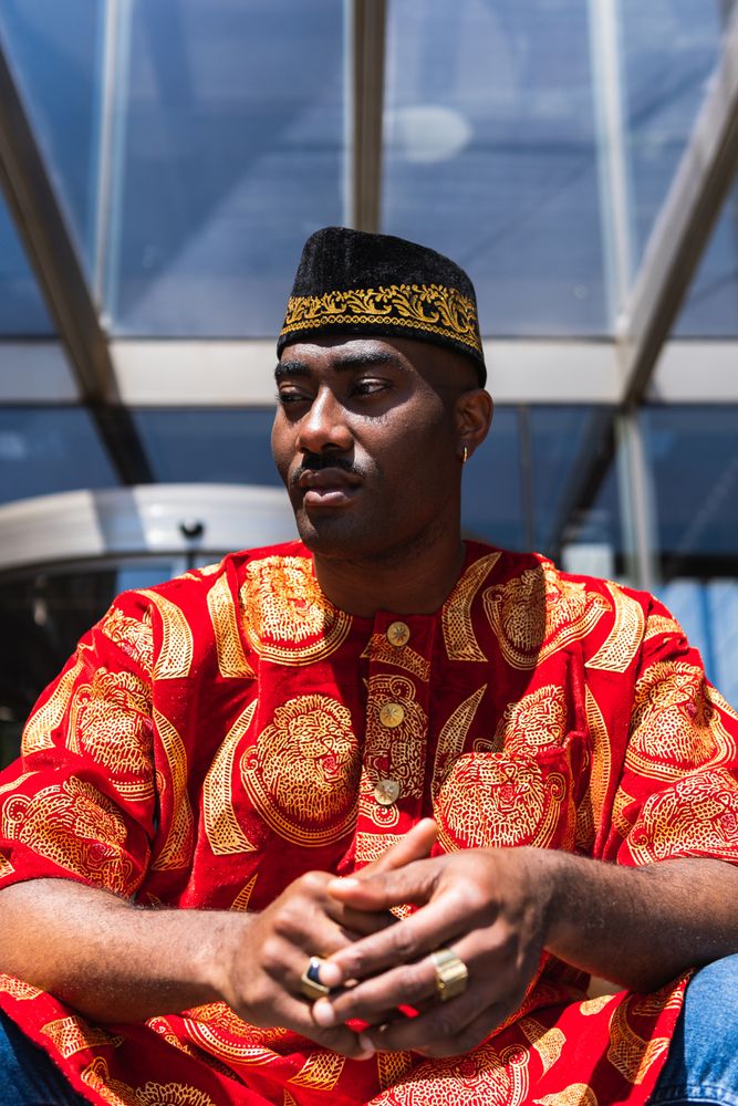 Thoughtful Black man in traditional clothes and headdress near building