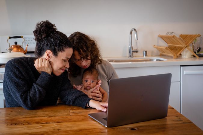 Two moms working on laptop at kitchen table with baby