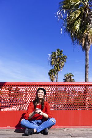 Woman in red sitting cross legged using a mobile phone outdoors on a sunny day