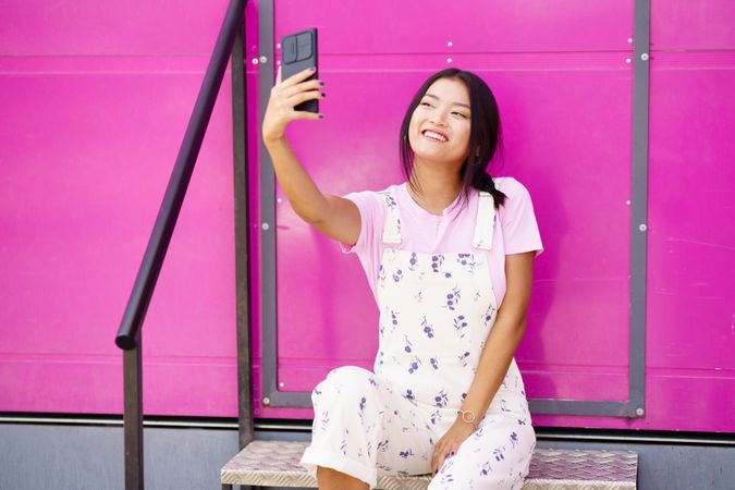 Smiling Chinese woman talking on video call on smart phone  sitting in front of pink trailer