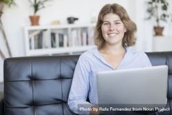 Happy woman sitting on a sofa at home working on a laptop 41laKO