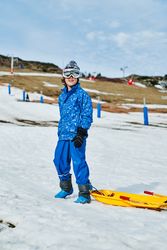 Kid with sleigh standing on snowy slope
