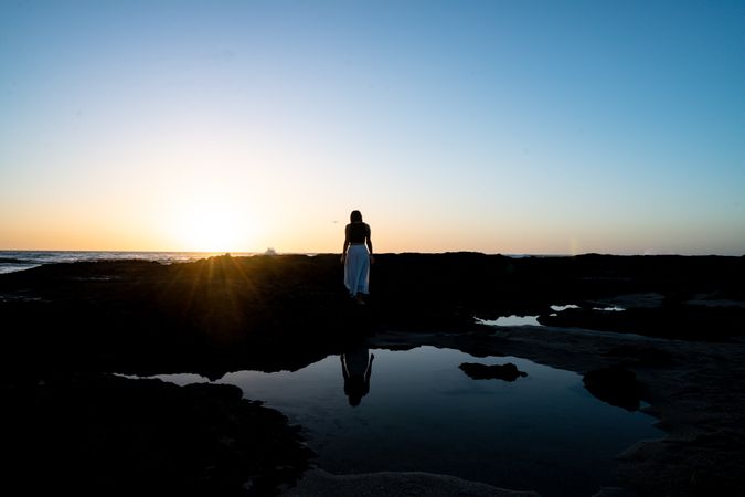 Woman standing on rock near body of water during sunset