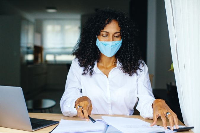 Woman in facemask holding a pen and working on documents