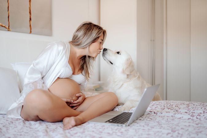 Cheerful pregnant woman using laptop and hugging dog
