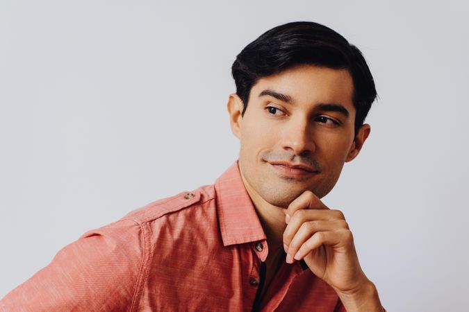 Headshot of curious Hispanic male looking away from camera in grey studio, copy space