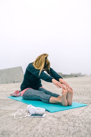 Young woman stretching legs by sea pier