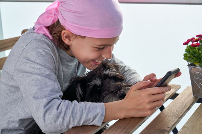 Happy child in bandana with dog using cellphone at table