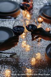 Two hands holding wine glasses cheers over a set dinner table 4BaOx5
