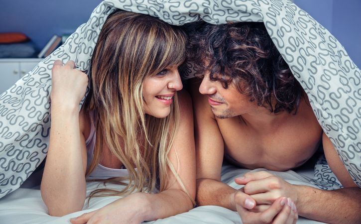 Happy young couple in love smiling under duvet cover