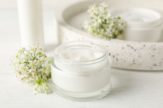 Cosmetic cream, tray and allium flowers on wooden background, space for text