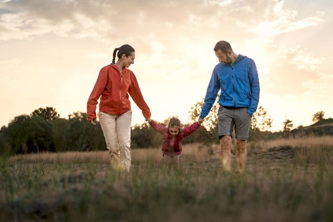 Happy family holding hands and walking together in a field at sunset.