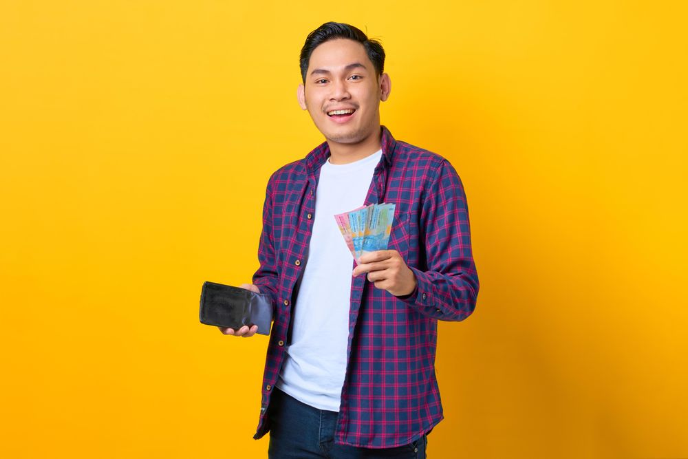 Smiling man holding cash out of his wallet