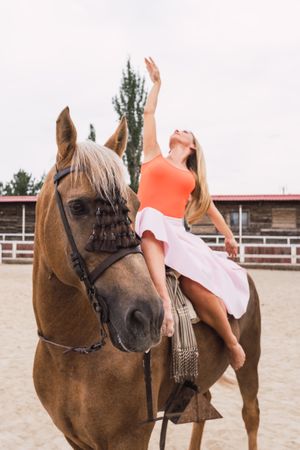 Graceful rider sitting at harnessed horse walking along paddock