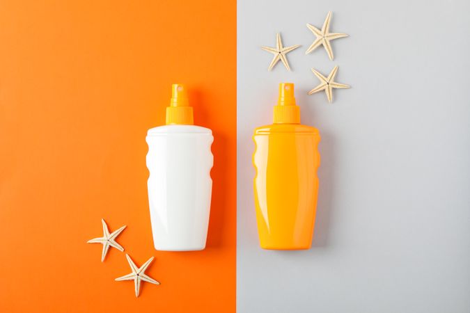 Flat lay composition with sunscreen sprays and starfishes on two tone background, space for text. Summer vacation backdrop
