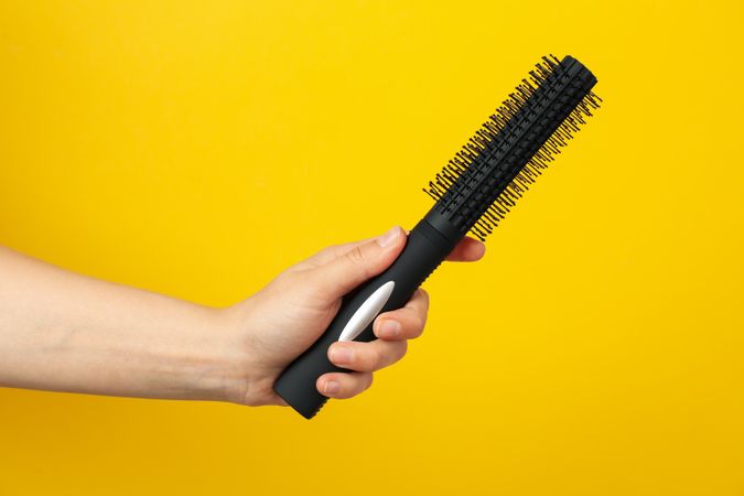 Female hand holds hair brush on yellow background, space for text