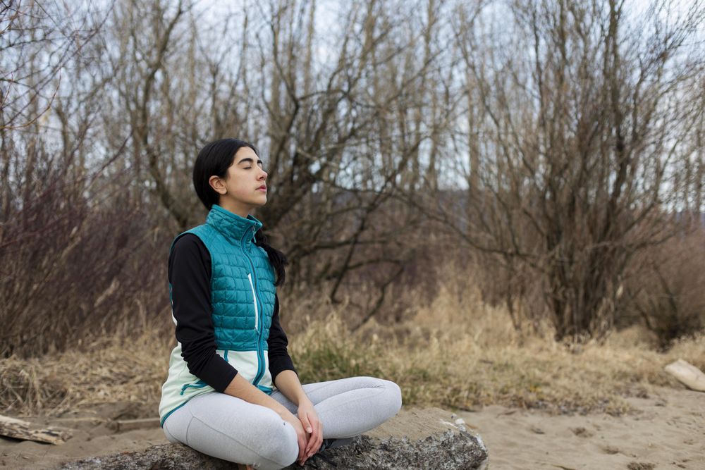 Young female peacefully sitting on a log while meditating