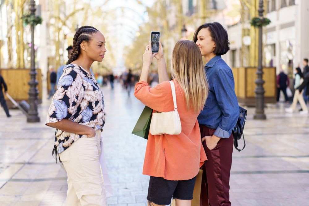 Three women taking picture on street with phone