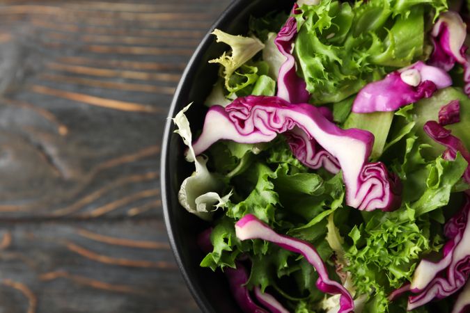 bowl with fresh vegetable slices on wooden background, close up