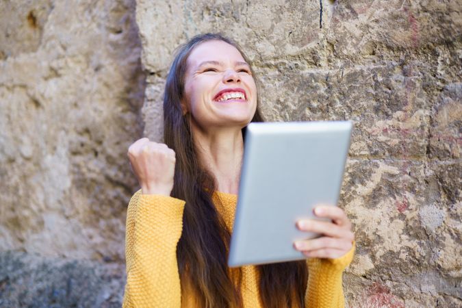 A Joyful Young Woman is Celebrating with a Tablet in Her Hand, Radiating Happiness and Enthusiasm