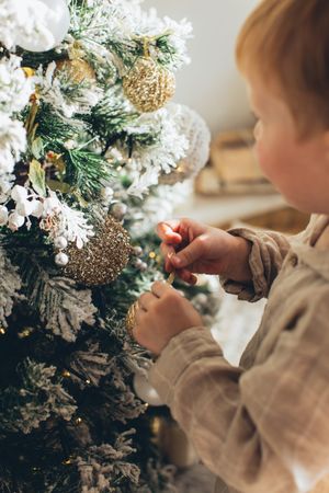 Cropped image of a baby standing beside Christmas tree decorated with gold baubles