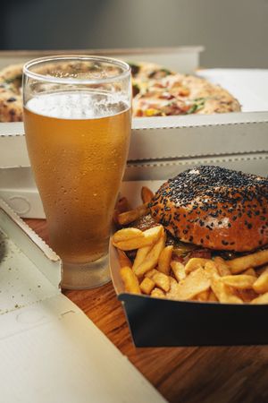 Burger, fries, pizza, and cold beer served on a wooden table