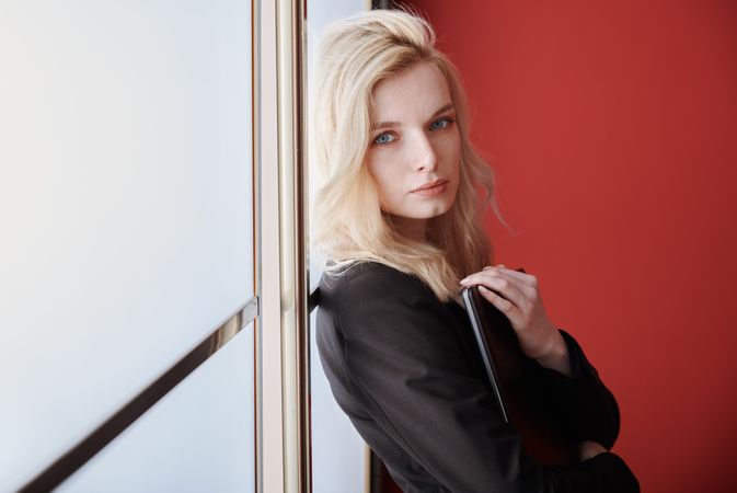 Young adult business woman standing next to the window holding phone