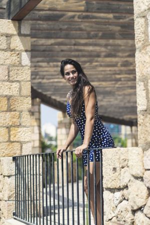 Hispanic woman in blue dress leaning over rail outside, vertical