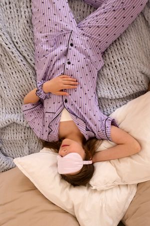 Girl lying upside down on bed with sleep mask.