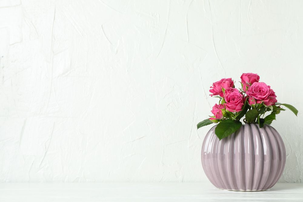 Vase with pink roses and space for text on table against light background