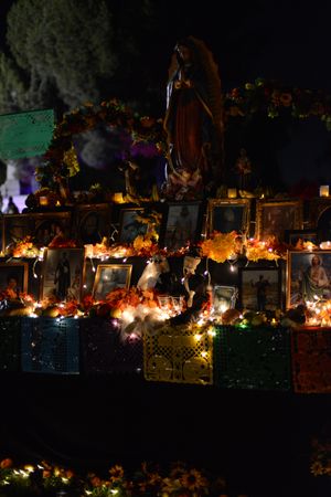 Day of the Dead altar at night with flowers, photos and lights