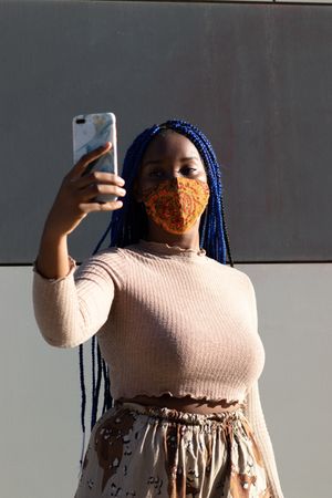 Stylish Black woman taking selfie in mask