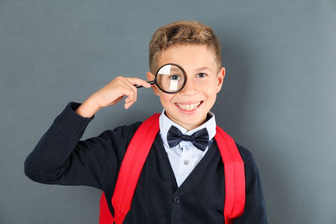 Boy in school uniform with magnifier against board, space for text