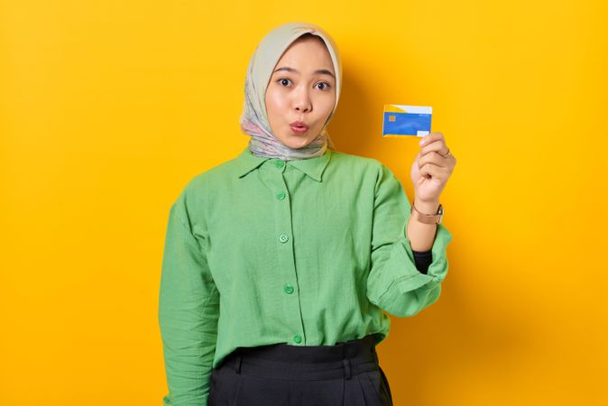 Surprised Muslim woman in headscarf and green blouse holding credit card