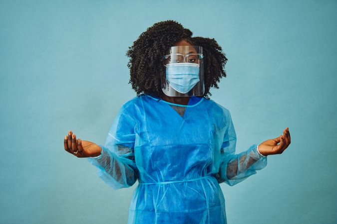 Black female doctor professional in surgical PPE, eye mask and shield, with arms stretched out