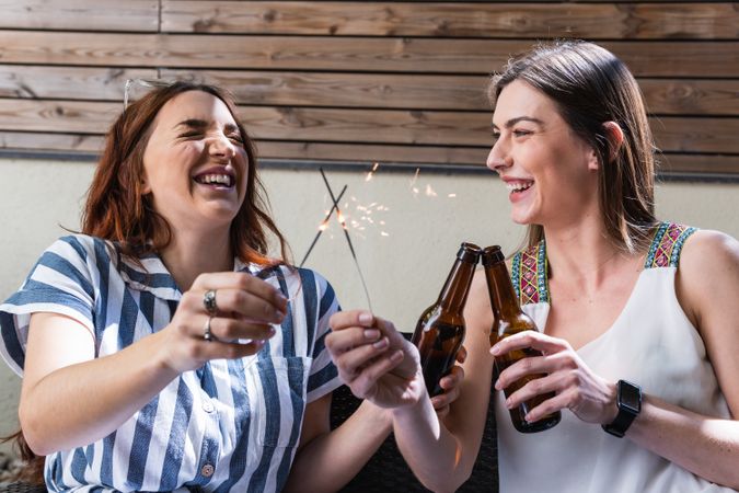 Joyful women clinking beer bottles and burning Bengal lights