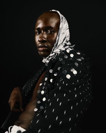 Side view of man in polka dot top and headscarf sitting against dark background